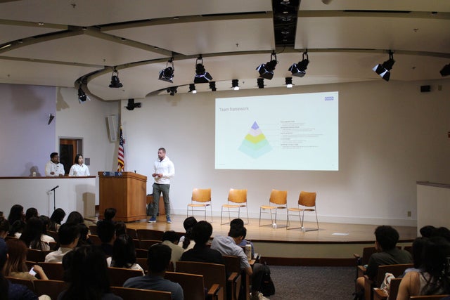 A man speaking to audience in an auditorium.