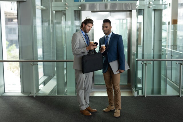 Two men in front of an elevator looking at a phone