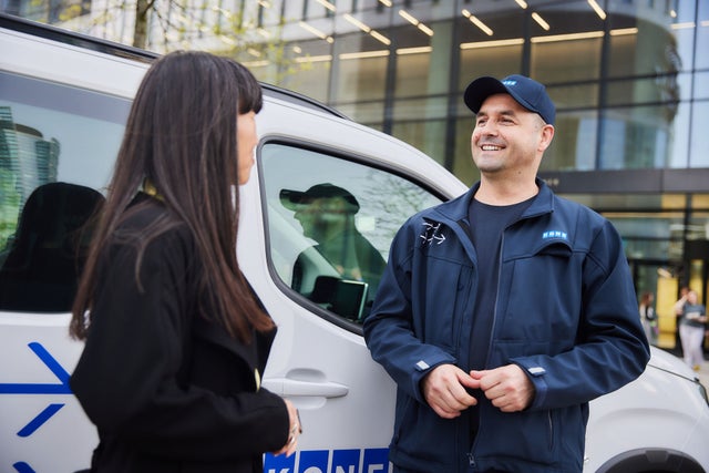 Nainen ja KONE-teknikko keskustelevat auton edessä.