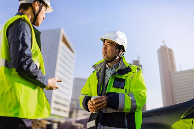 Two construction site employees in safety gear discussing with one another