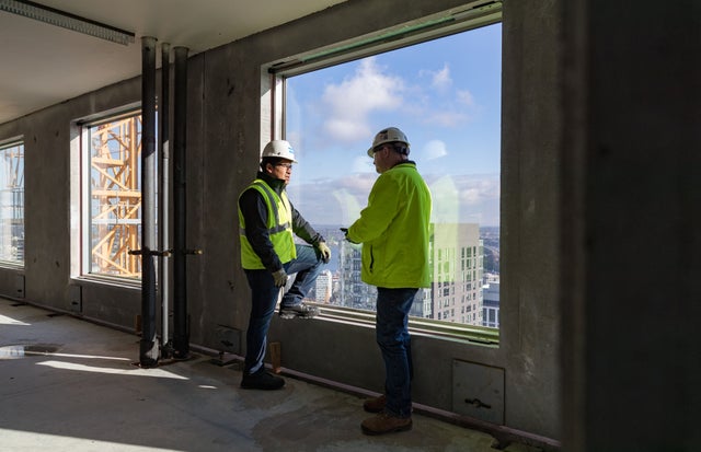 Two people talkin in front of a window in a construction site.