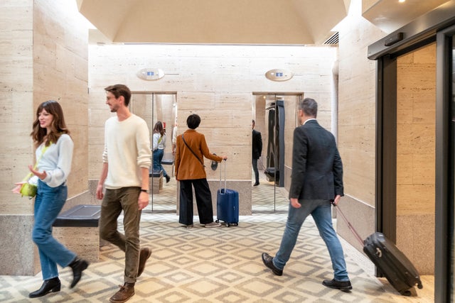 People walking in a lobby, elevators in the background.