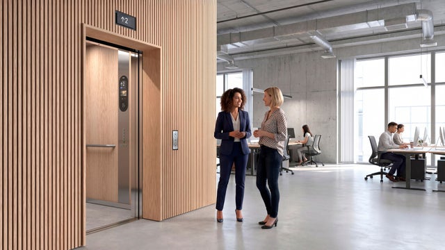 Two women standing in front of an open elevator with an info screen