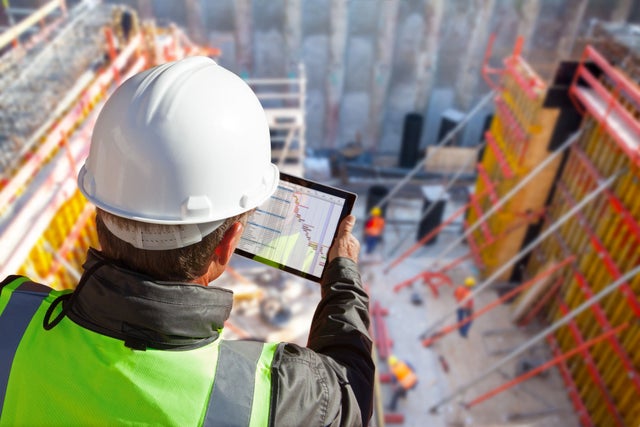 civil engineer or architect with hardhat on construction site checking schedule on tablet computer.