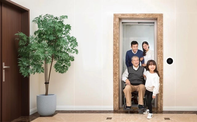 A family coming out of a home elevator pushing an older man in a wheelchair