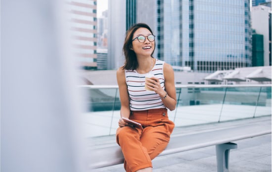 woman sitting outside with coffee with buildings in background