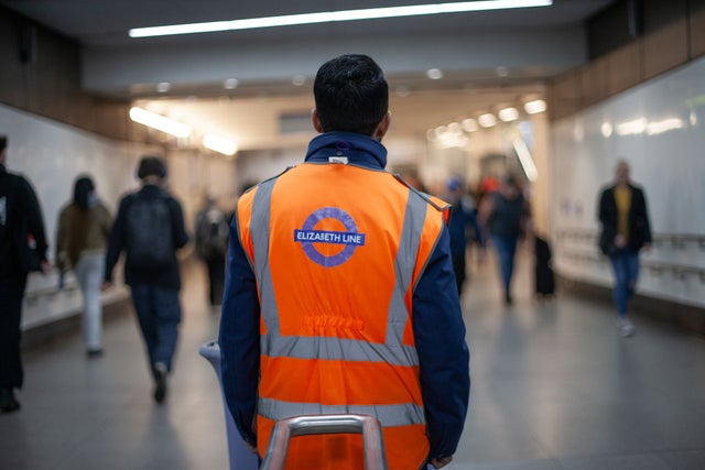 A person wearing an orange vest that says Elizabeth line standing backwards to the camera