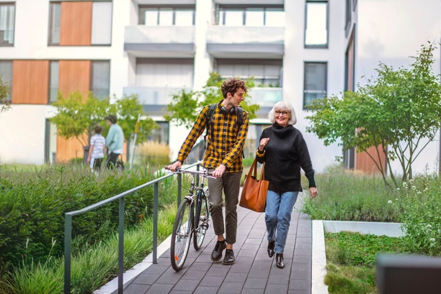 Young man with bike and a woman walking in front of residential building