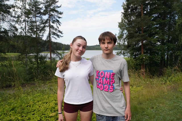 A young girl and a boy standing in a green scenery.