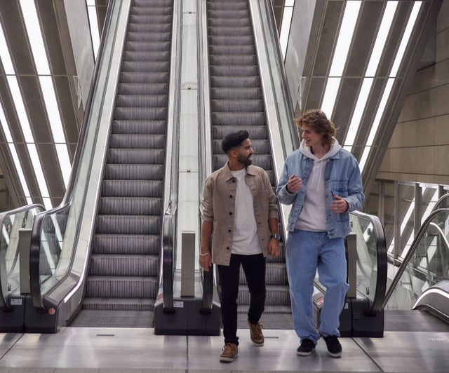 Two men at the end of an escalator looking at each other.