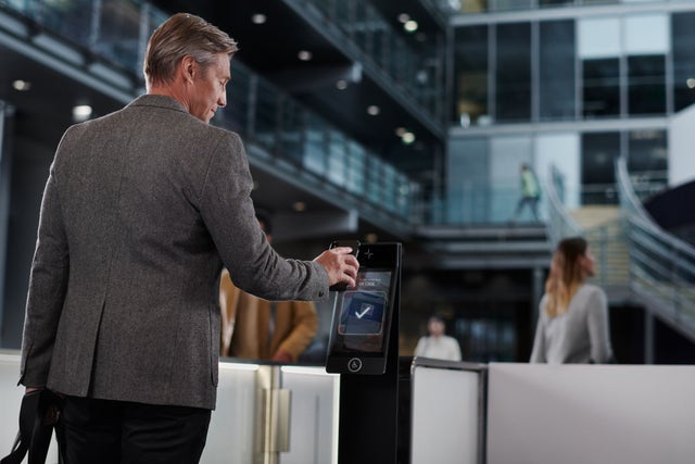 A man walking towards a turnstiles and showing a code from the phone to a machine.