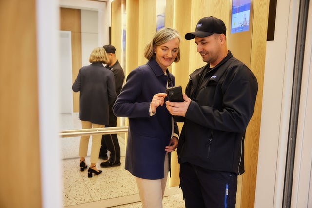 KONE technician showing a mobile app to a woman inside an elevator.