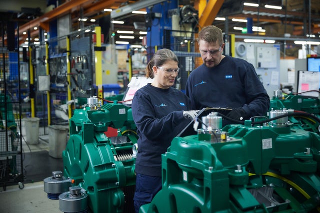 Two people working with a hoisting machine in a factory