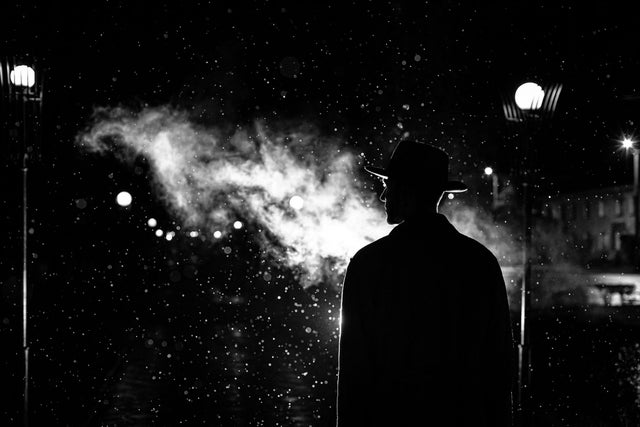 A black and white picture of a person facing back at the camera looking to the left. In front of them is smoke.
