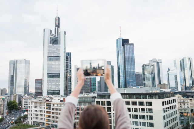 Woman taking a picture of a city skyline with a small tablet computer.