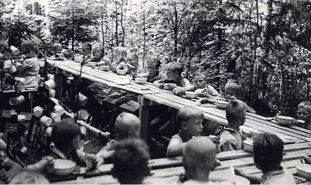 Children eating lunch outside in an old black & white photo.