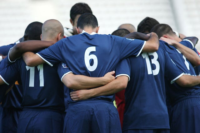 Male athletes huddling on sports field.