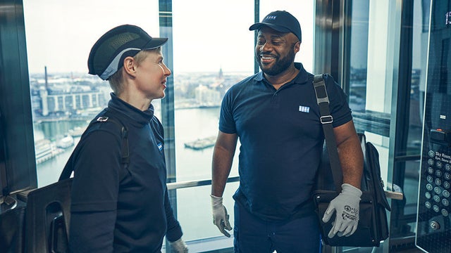 Two KONE technicians smiling in a high-rise elevator.
