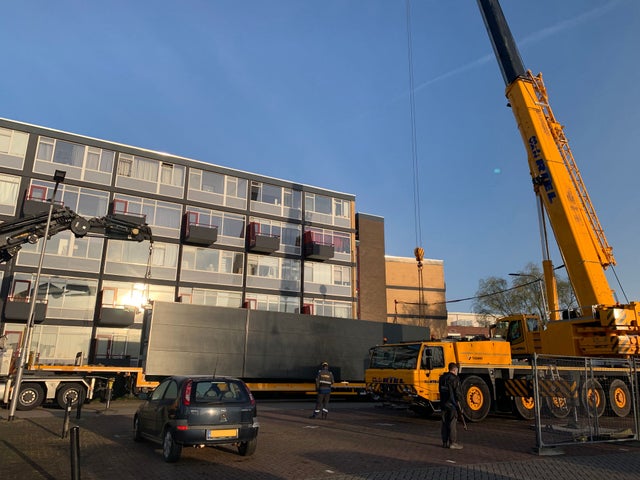 A mobile crane lifting an elevator outside a residential building.