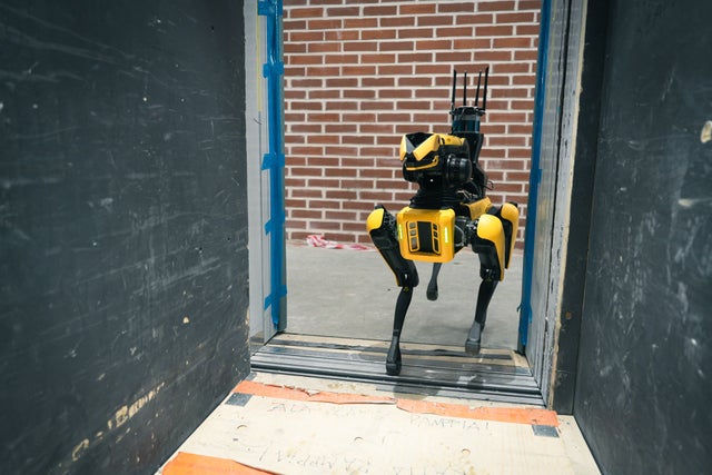 A yellow and black colored spot the robot dog walking inside an elevator.