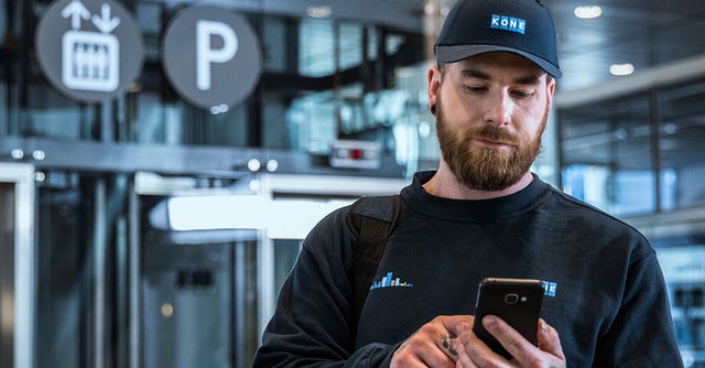 KONE technician checking the mobile phone, elevator in the background.